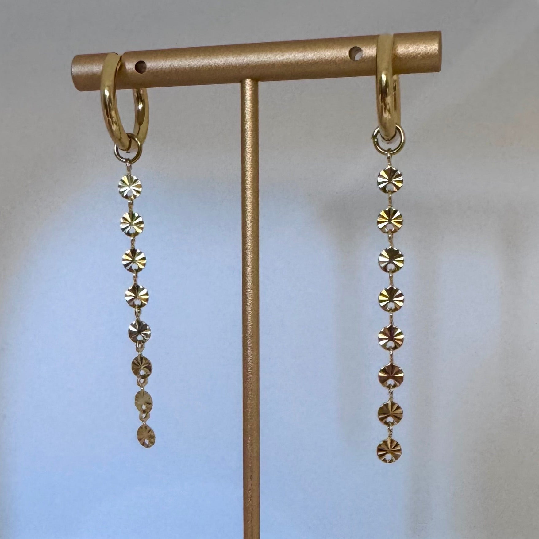 Gold earrings with disc-shaped beads on a gold stand against a light beige background