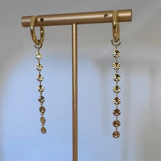 Gold earrings with disc-shaped beads on a gold stand against a light beige background